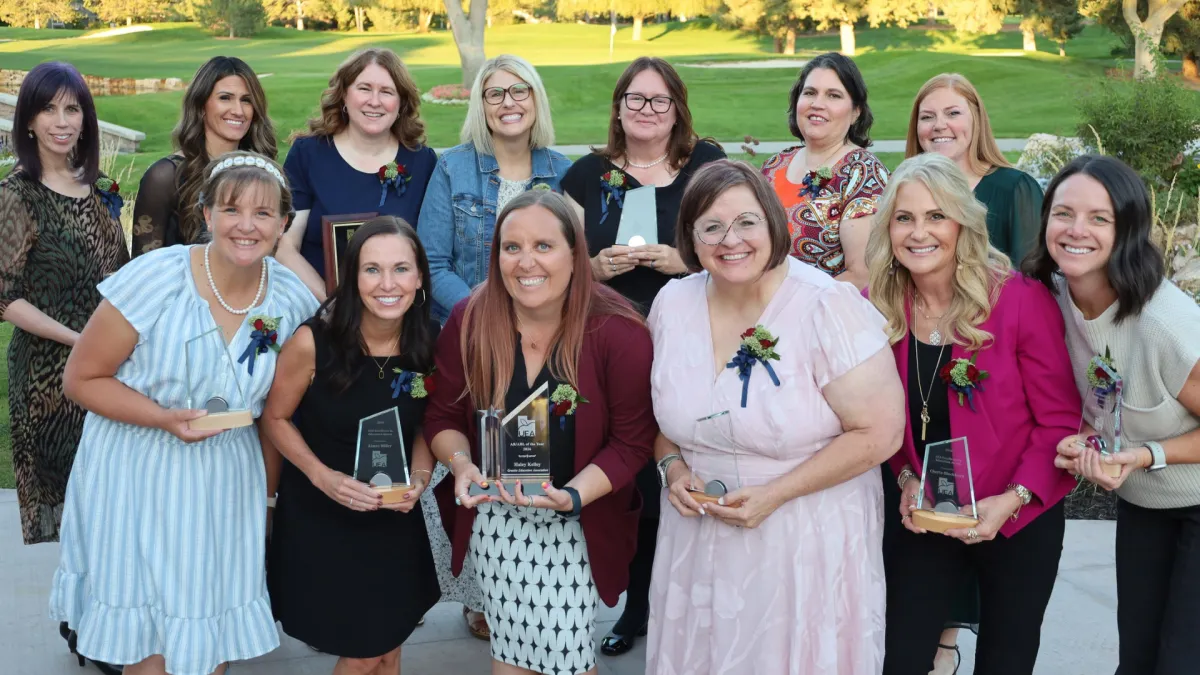 Group of 13 women holding trophies smiling while outside. 