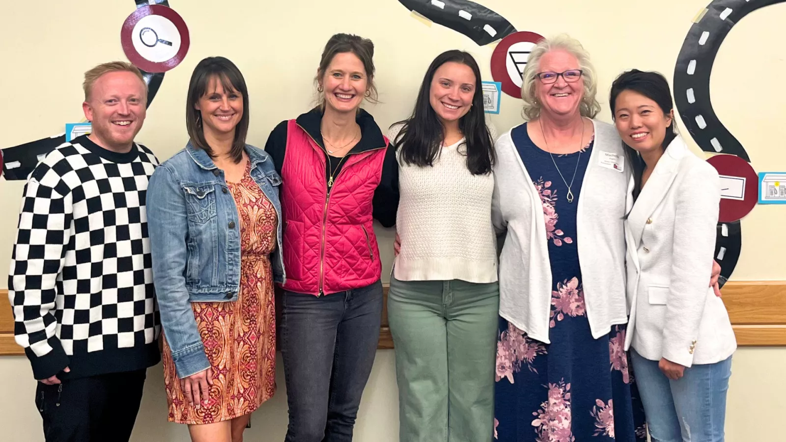 Six smiling educators in a row standing in front of a wall.