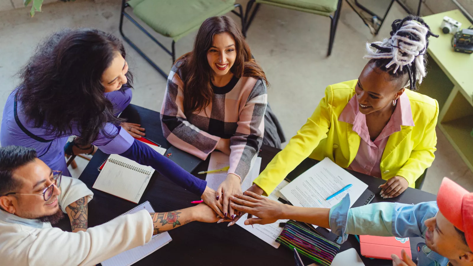 Five people sitting at a desk giving a high five and smiling.