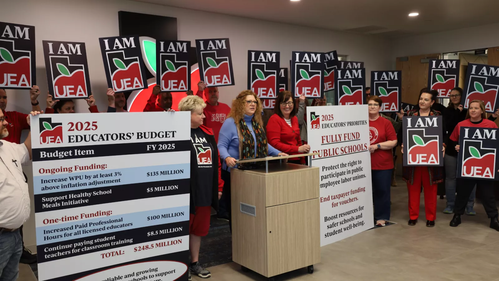 President Pinkney at podium with people holding signs around her. 