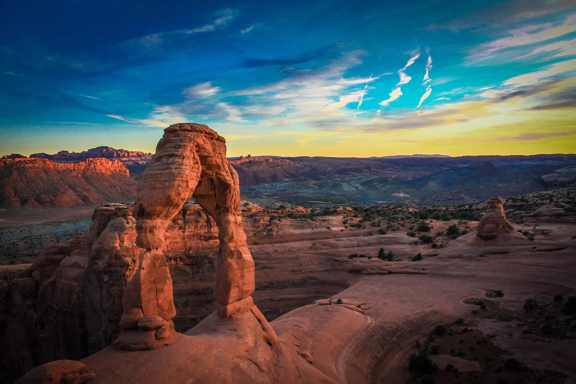 A natural rock arch in the middle of a setting sun scene.
