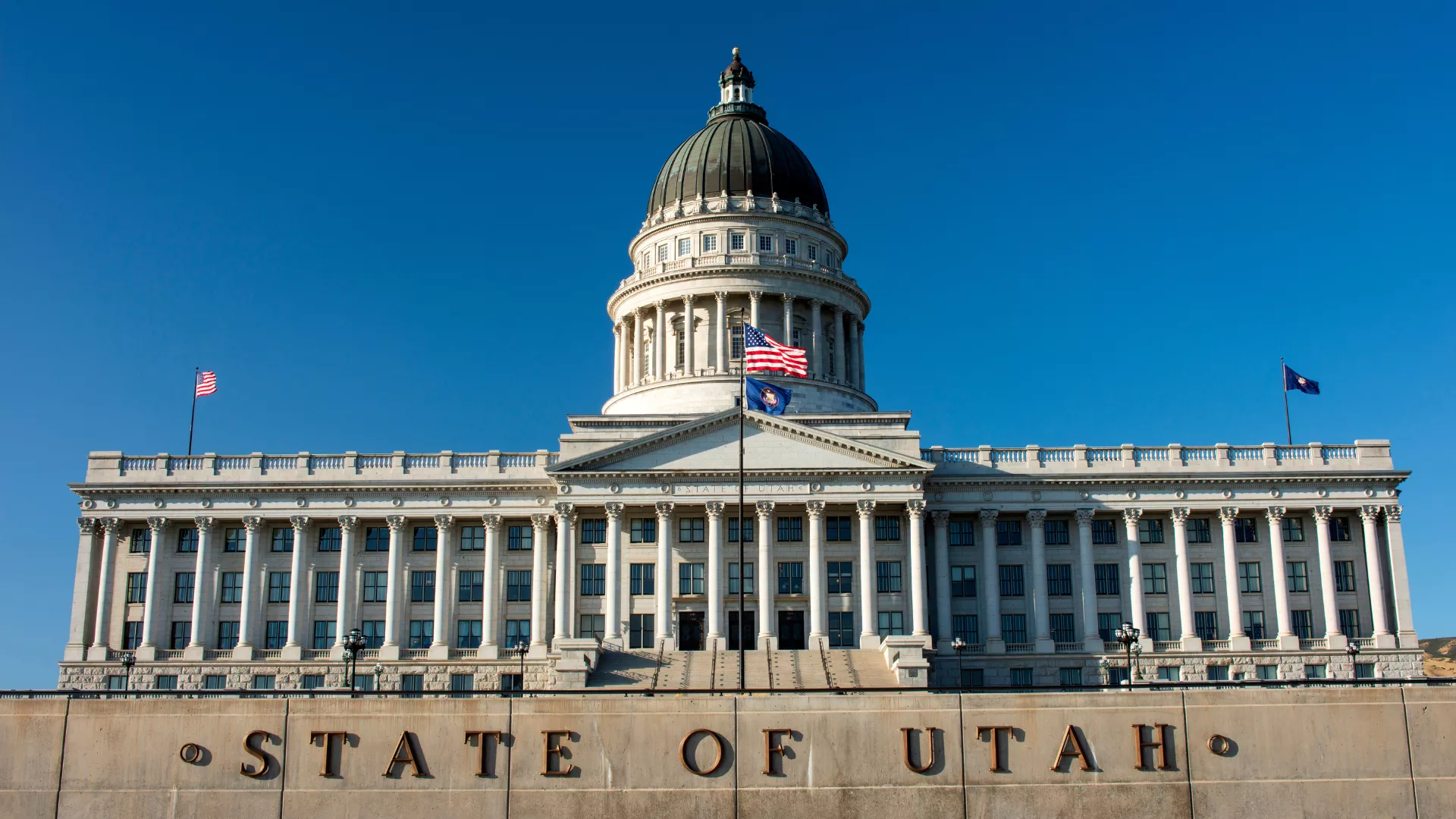 The front of the Utah capitol with a bright blue sky with the words State of Utah in the foreground.