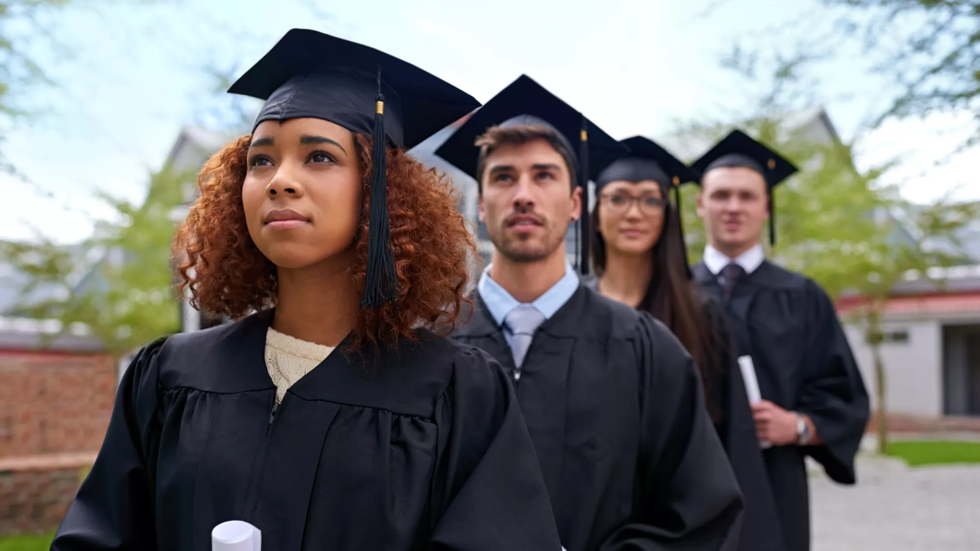 College students wearing caps and gowns in a row looking inspired. 
