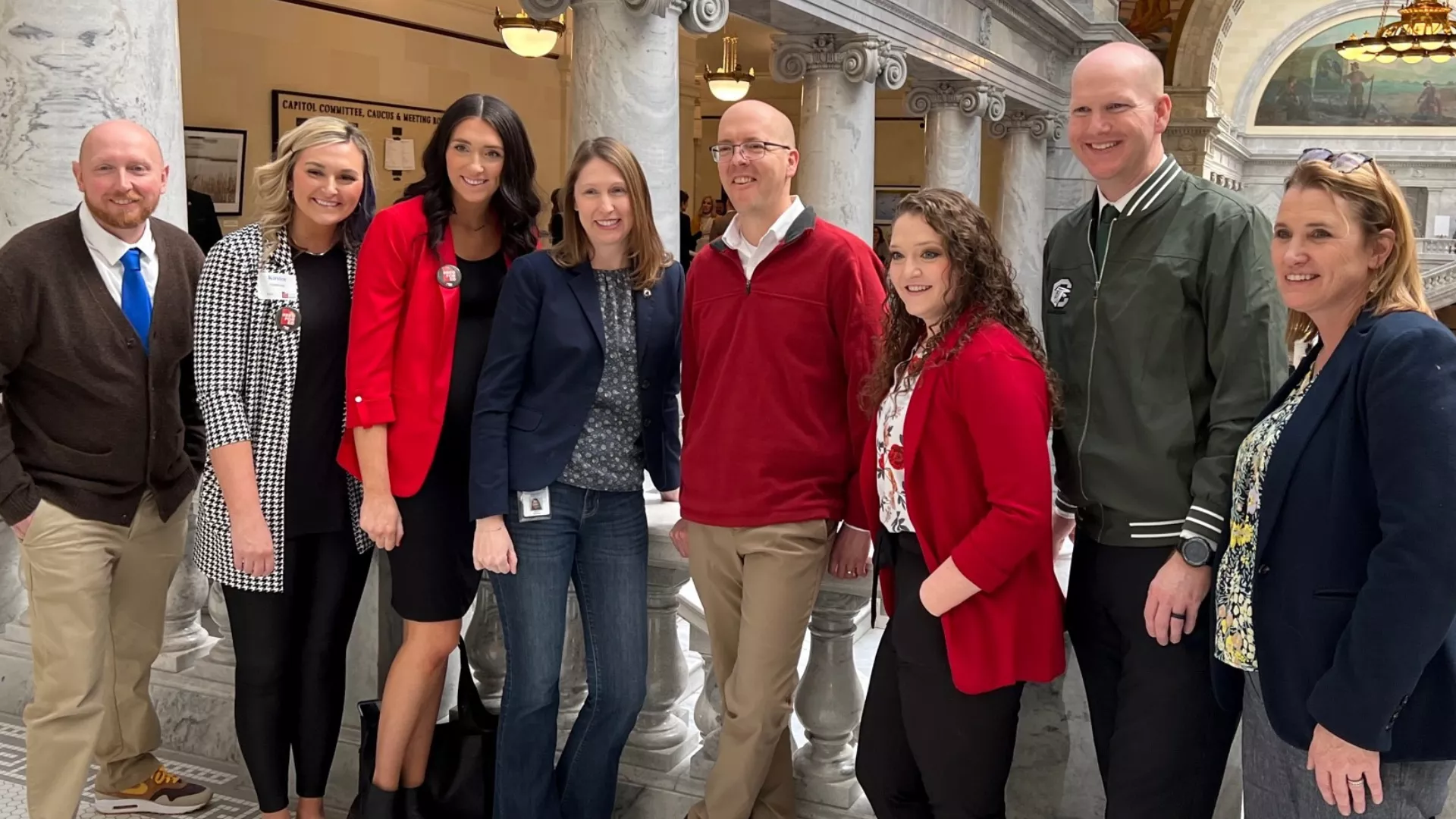 Eight people smiling in a row in the capitol rotunda. Many wear red.