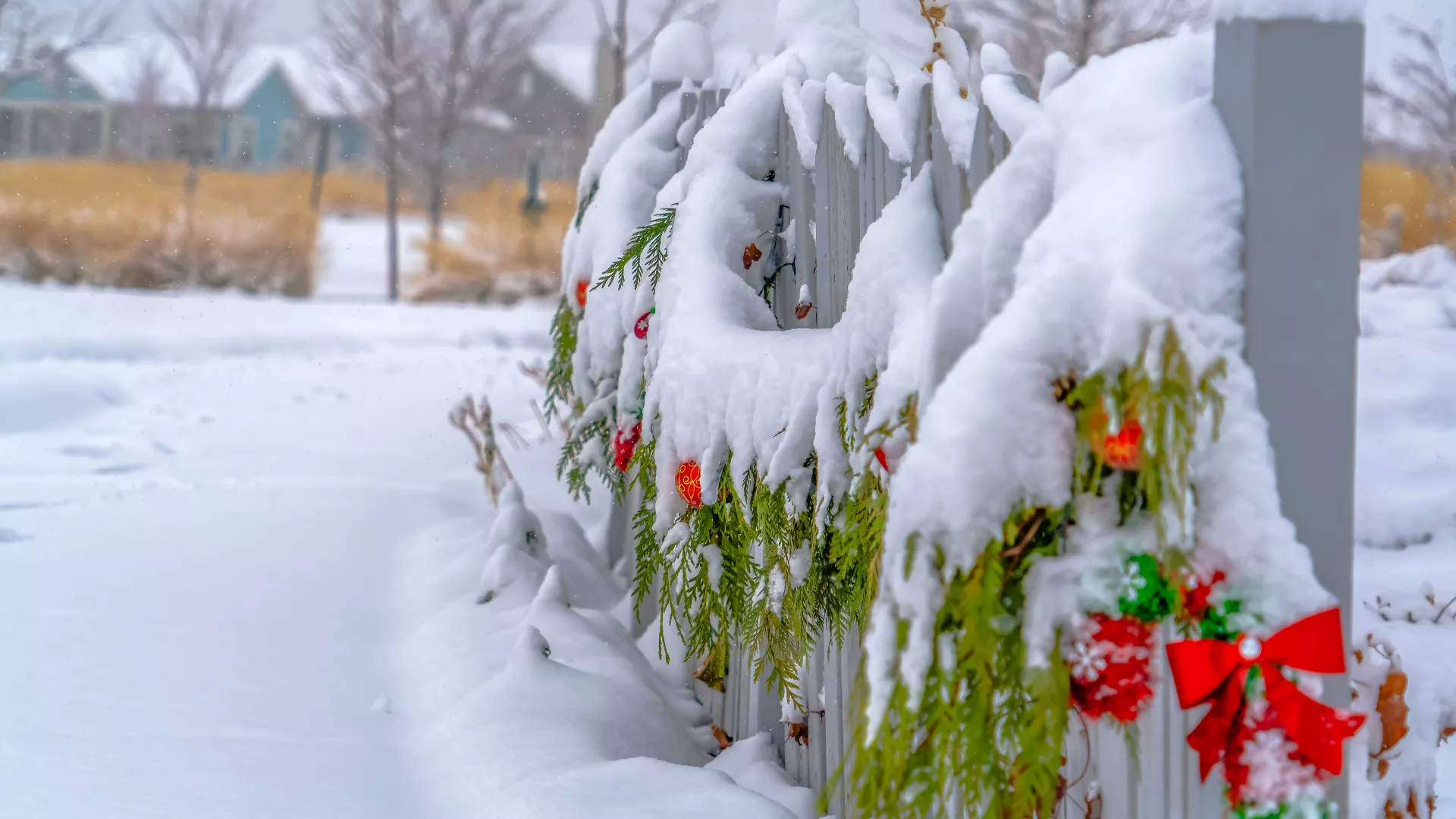 Snow on outdoor holiday ornaments and greenery hanging on a fence.