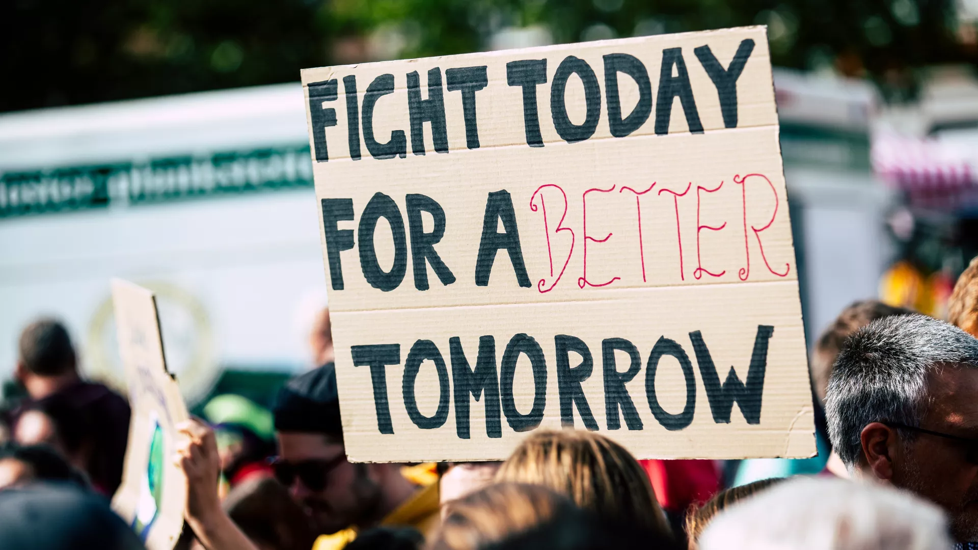 Cardboard sign raised above group of people reads, "Fight today for a better tomorrow."