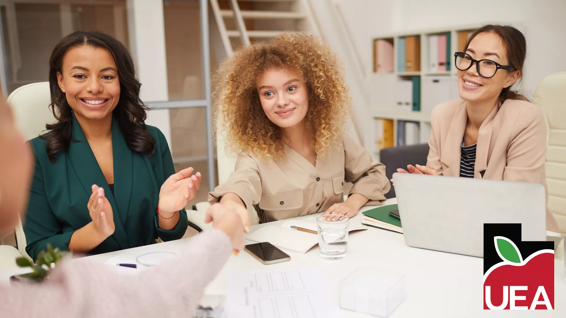 Three women sit across the table and shake a man's hand.