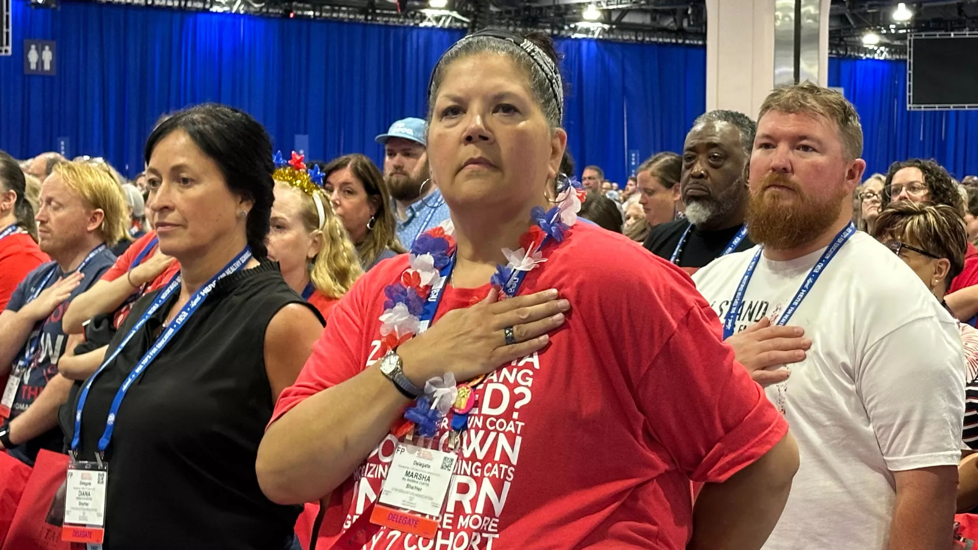 White woman wearing red shirt hold her hand on her chest out of respect for the US flag.