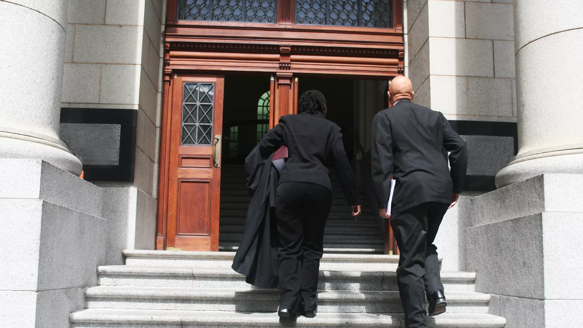 Two people in suits walk up the steps of a courthouse.