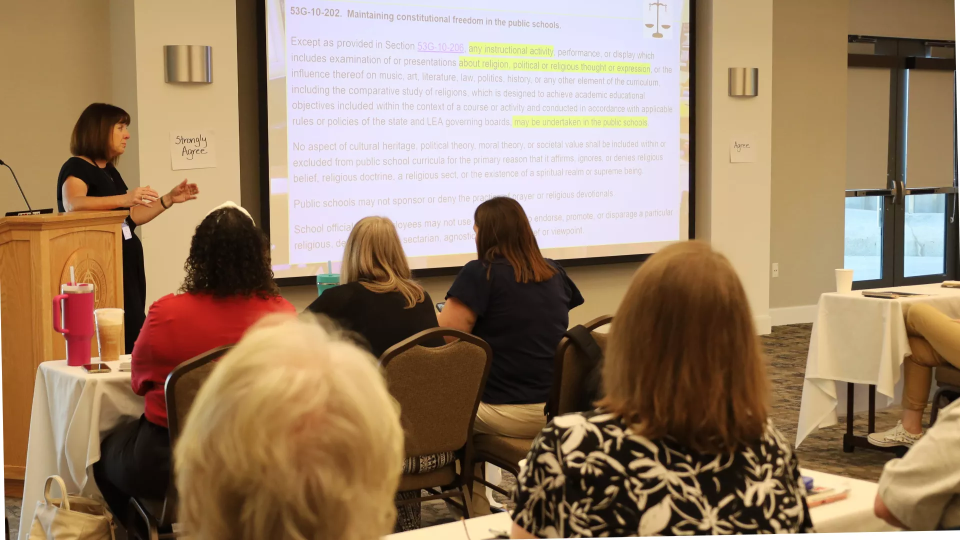 Woman stands at podium and teaches a group of UEA members.