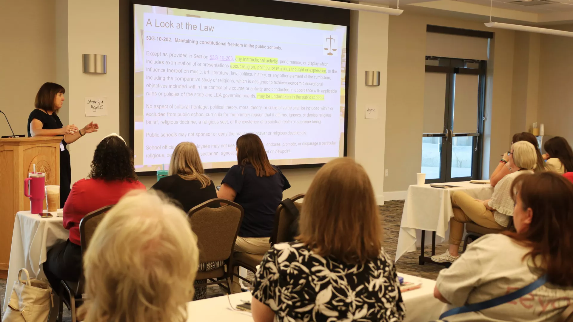 Woman stands at podium and teaches a group of UEA members.