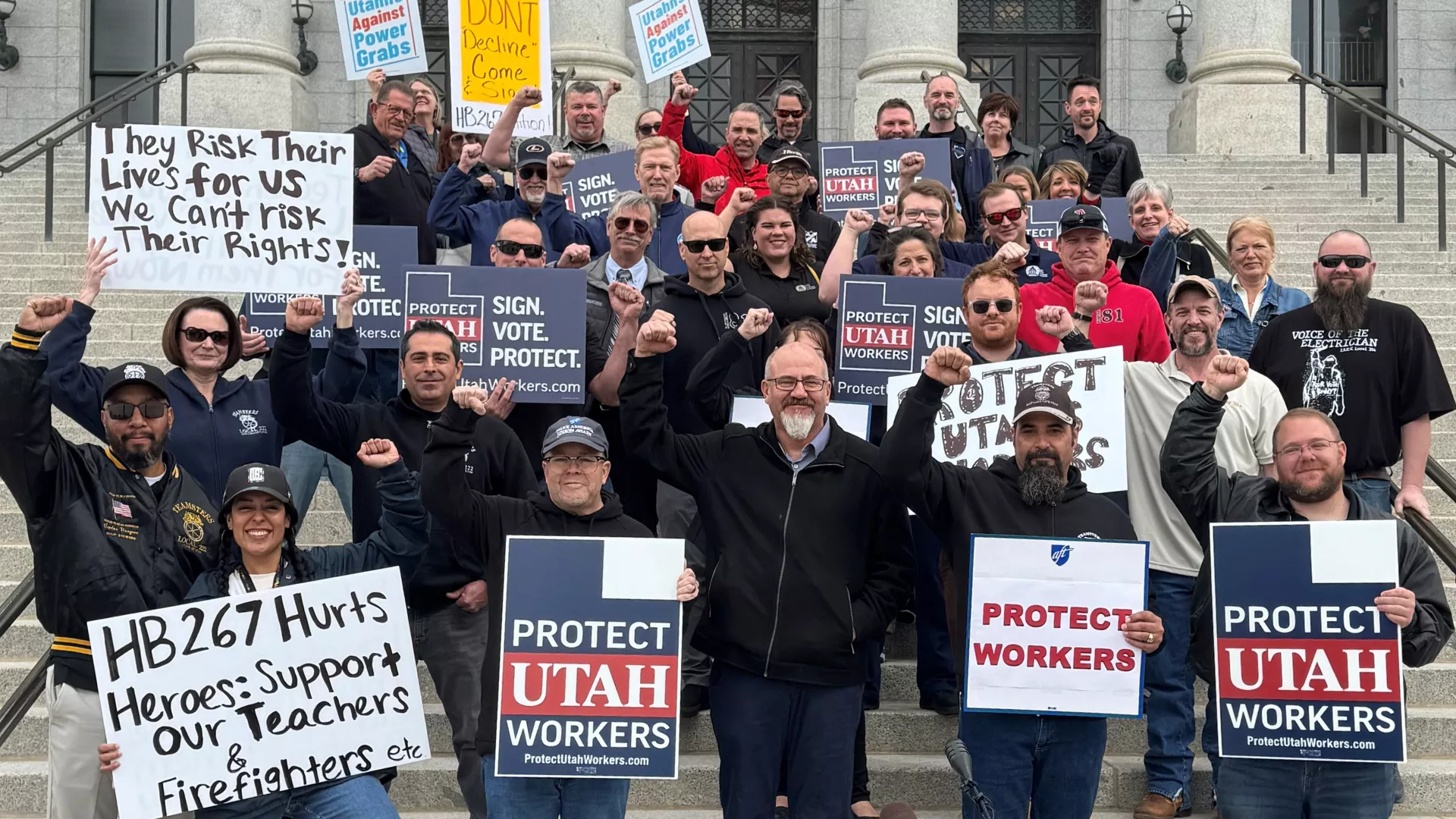 Group of people on capitol steps holding signs.