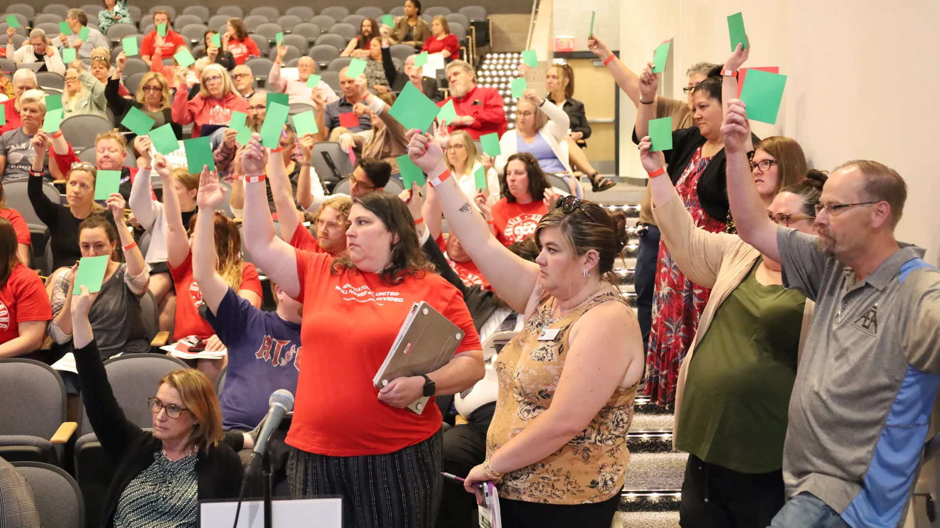 Group of educators hold up green cards during vote.