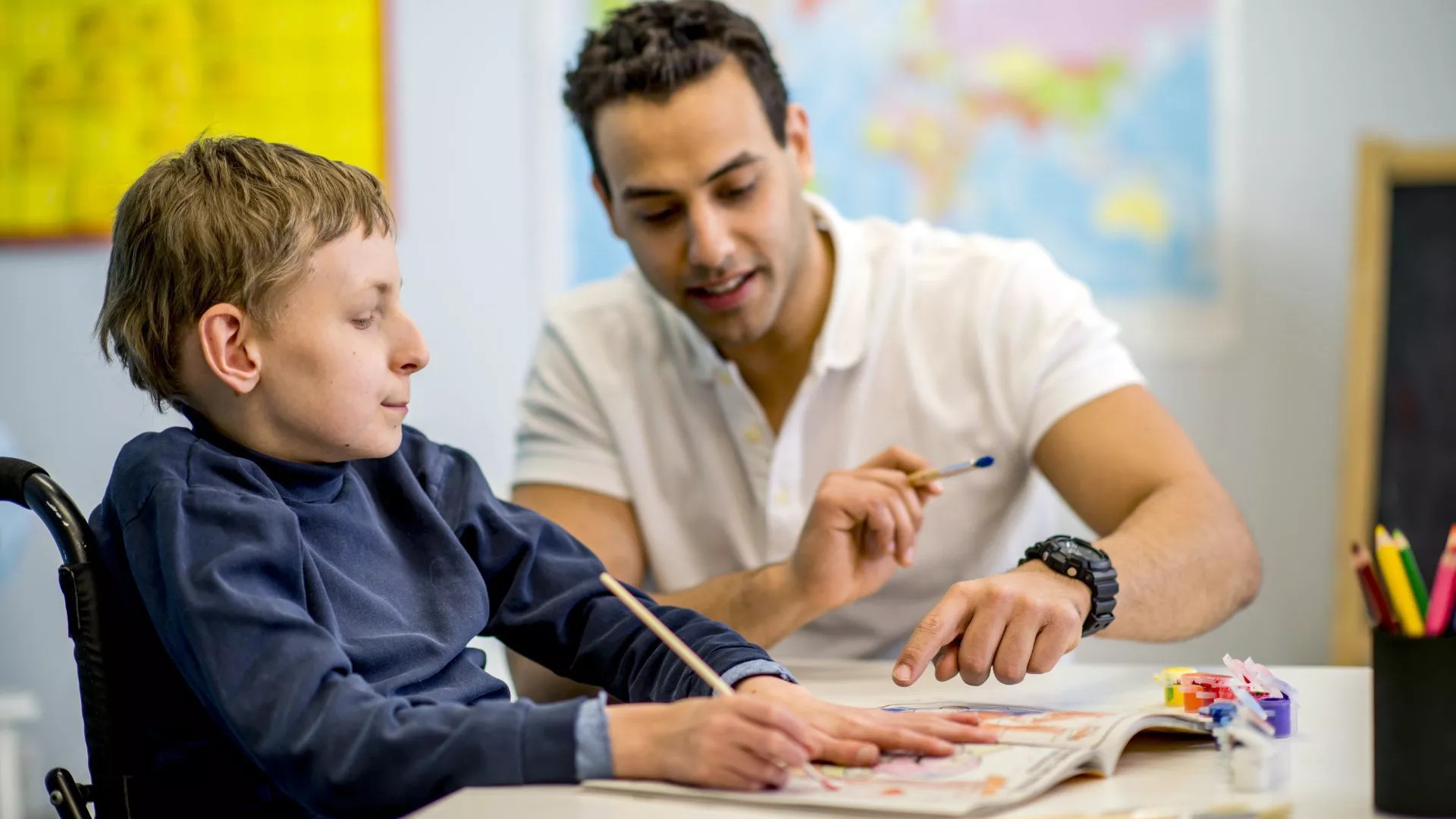 Child in wheelchair working with a teacher at a desk