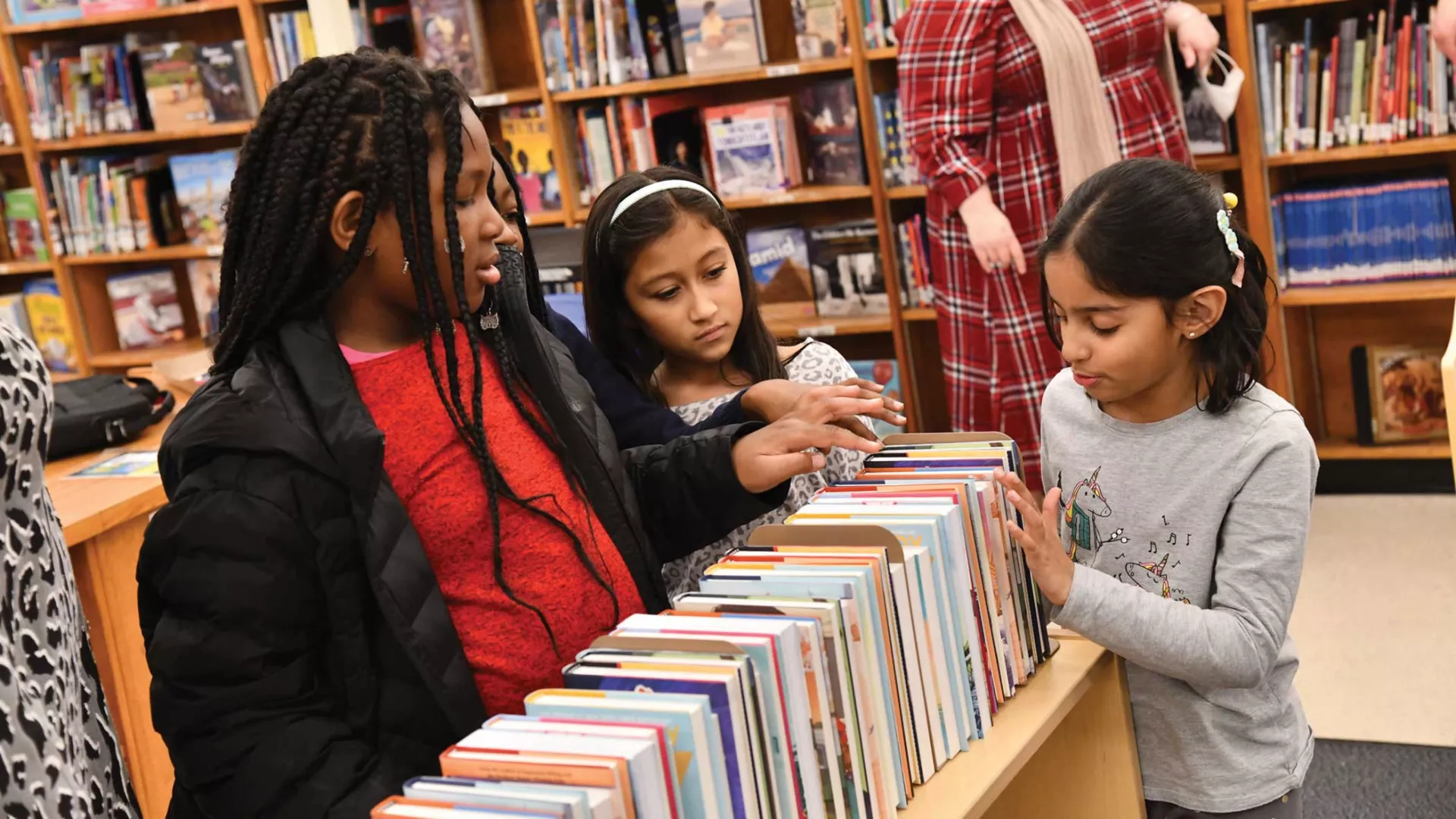 Black female educators helping two young female students of color at a library