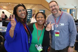 Three UEA staffers smiling at the camera, two hold up peace signs. 