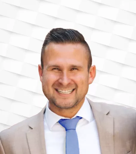 White man against a white background smiling wearing a suit and tie.