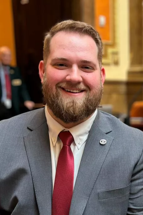 Man in grey suit and red tie smiles while at the Utah Capitol.