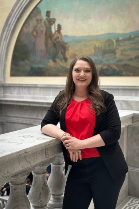 Dark haired woman wearing a red blouse leans on a granite railing at the capitol. 
