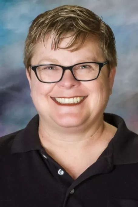 Woman smiling with a blue-grey background wearing a black jacket