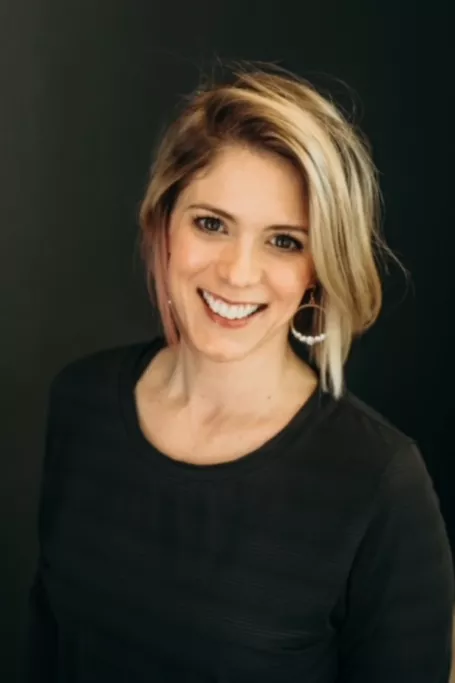 Blonde woman with black shirt smiling against black background.