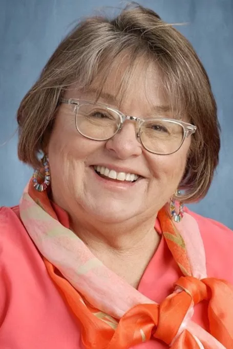Woman wearing pink smiles in school picture.