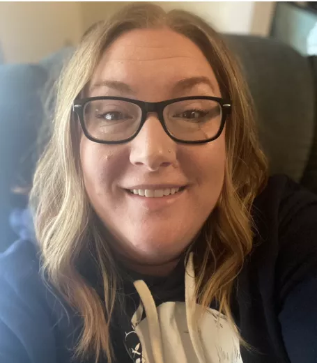 White woman with blonde hair and glasses.