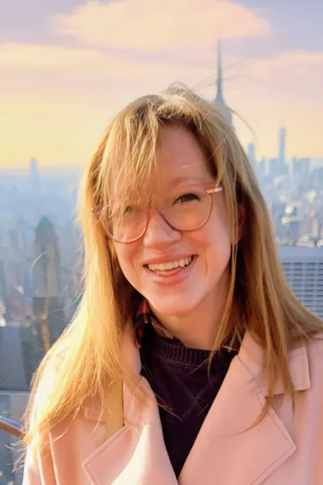 Woman with pink coat smiling with city skyline in the background.