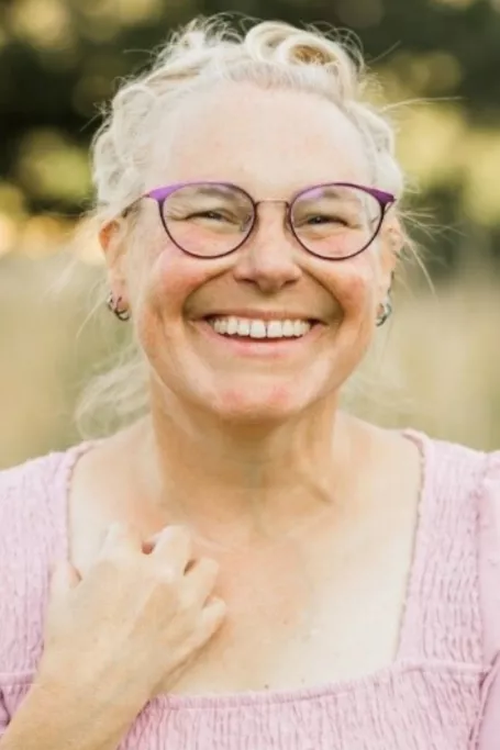 Woman with pink top smiles with glasses.