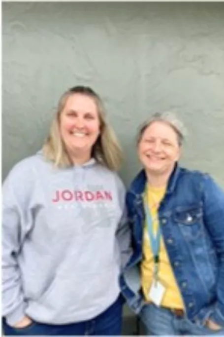 Two woman smiling against grey backdrop.