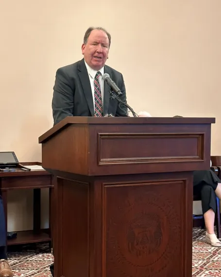 Man in grey suit stands at wood podium. 