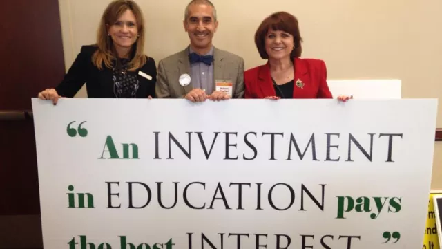 Former Teachers of the Year pose with a sign that says "An investment in education pays the best interest."