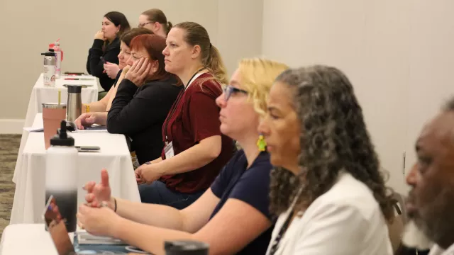 Row of educators listening to a presentation sitting at a table.