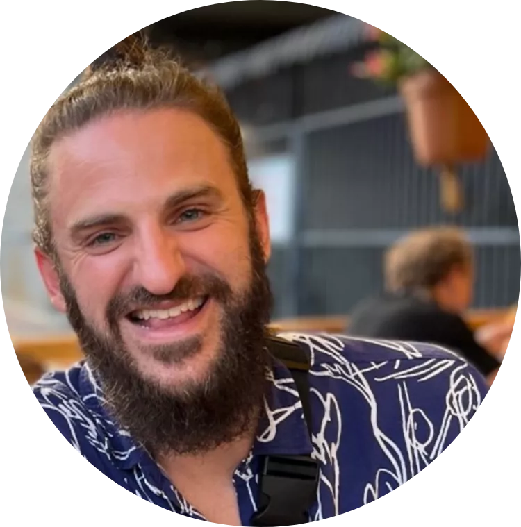 White man smiling with beard wearing a blue and white shirt.