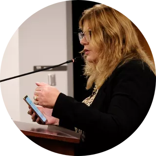 President Renee Pinkney stands at podium speaking to Utah State Board of Education with phone in her hand. 