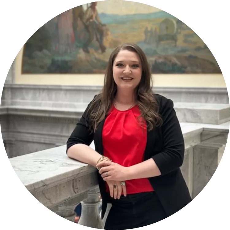 Dark haired woman wearing a red blouse leans on a granite railing at the capitol. 